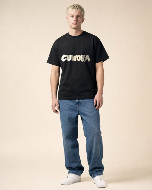 Model wearing the CUWORA Wordmark Tee in Black, front view with the bone CUWORA wordmark across the chest